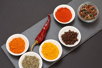 Various ground spices and herbs on stone cutting board.
