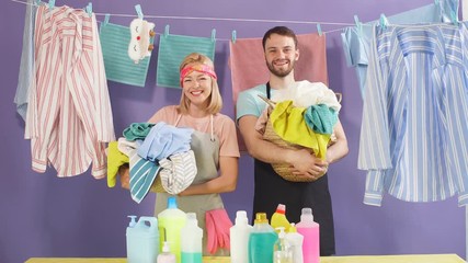 Hardworking attractive couple holding basket of laundry and looking camera. Household chores clean clothe hanging on clothesline