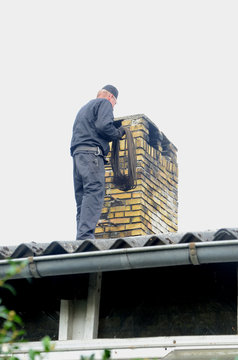 Chimney sweeper at work on a roof with a yellow stone chimney