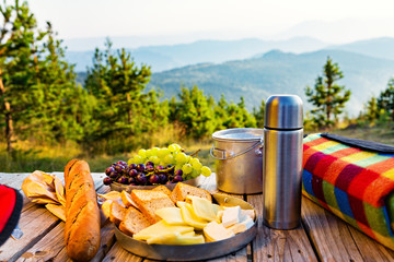 Small snack in the mountains. Cheese, grapes and baguette on top of wooden table, with mountains in the distance.