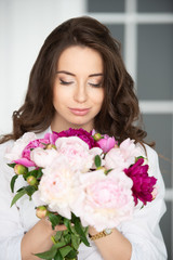 Close-up portrait of a beautiful young woman girl with gorgeous hair and a bouquet of peony flowers.