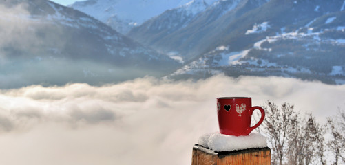 Naklejka premium view on a red mug put on a snowy pole of a terrace above a sea of clouds in mountain