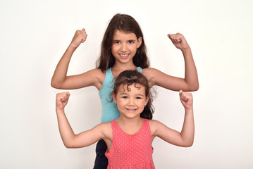 Cute smiling young sisters standing behind each other and showing their strong arms 