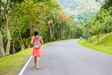 Fototapeta na wymiar Beautiful rainforest with a young woman traveler with a backpack on the road to the forest Thailand. A woman walks along a tropical road and enjoys the views of nature.
