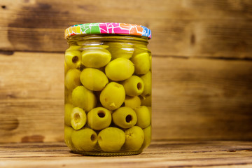 Pickled green olives in glass jar on wooden table