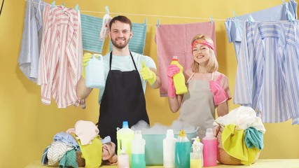 Happy couple holding bottles with cleaner liquid for washing clothes. Isolated yellow background, studio shot. Advertisement concept. Free time, spare time