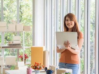 Portrait of a beautiful Asian businesswoman holding a laptop and looking at the camera with a smile while standing in the office