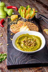 Hummus with spinach, avocado and pumpkin seeds in a bowl on a wooden board and bruschetta, oriental and Arabic cuisine , vertical orientation