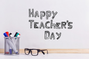 The inscription marker on a white board, Happy Teacher's Day. A table with glasses and attributes for writing.