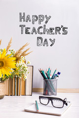 Bouquet of flowers and notebooks with eyeglasses on table. The inscription happy teacher's day..