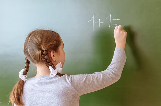 Schoolgirl solves a math problem on the blackboard during the lesson.