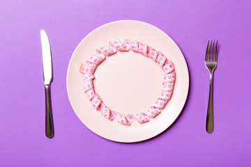 Measuring tape in a plate with fork and knife on both sides on purple background. Top view of weight loss concept