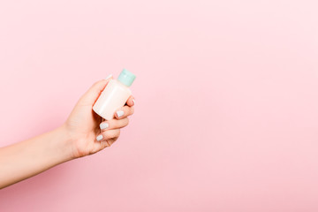 Obraz na płótnie Canvas Female hand holding cream bottle of lotion isolated. Girl give tube cosmetic products on pink background
