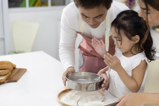 Happy Asian family Father, Mother and Daughter are sieving flour preparing the dough, bake cookies in the kitchen. family cooking food Concept. - Powered by Adobe