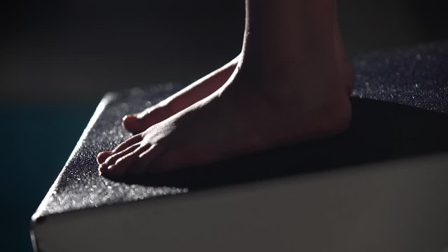 Close up shot of a professional female swimmer's feet preparing to jump off the starting block into the swimming pool. Night shot