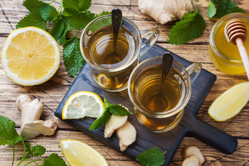 Two cups of natural herbal tea ginger lemon mint and honey on a wooden background.