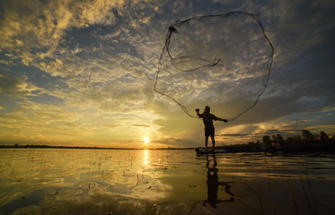 Silhouette of fisherman throwing fishing net during sunrise. Silhouette of man catching the fish in...