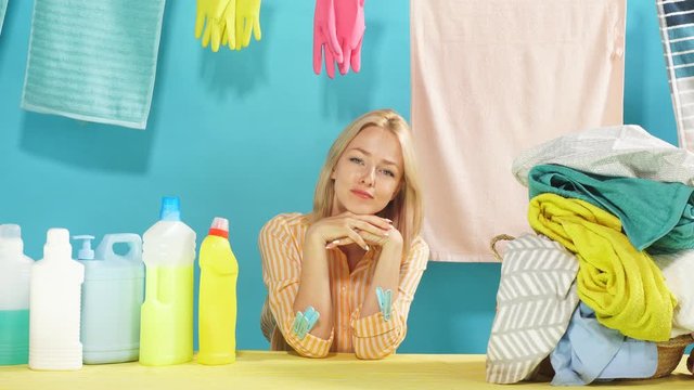 Cheerful blonde housemaid is rejoicing at good qualified detergent, isolated blue background. Woman has found effective wahing powder for dirty clothes