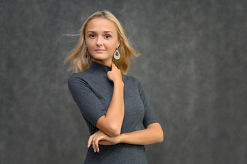 Studio portrait of a pretty blonde student girl, young woman in a gray sweater on a gray background. Talking, showing emotions.