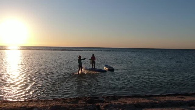 Aerial view on two young women in the sea, on surfboards, during sunset