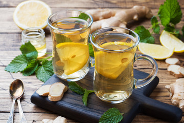 Two cups of natural herbal tea ginger lemon mint and honey on a wooden background.