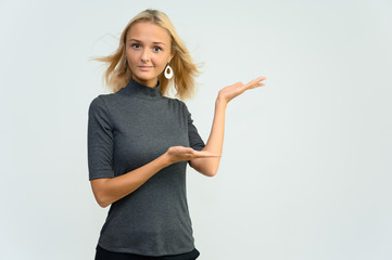 Studio portrait of a pretty blonde student girl, young woman in a gray sweater on a white background. Talking, showing emotions.