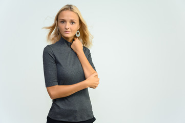 Studio portrait of a pretty blonde student girl, young woman in a gray sweater on a white background. Talking, showing emotions.