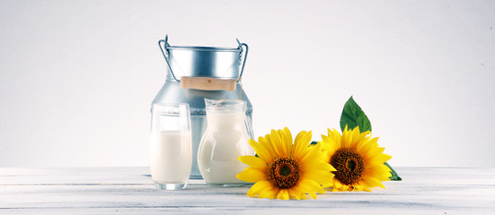 A jug of milk and glass of milk on a wooden table and flower