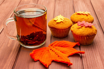 Hot autumn drink. Black tea with cupcakes, colorful leaves