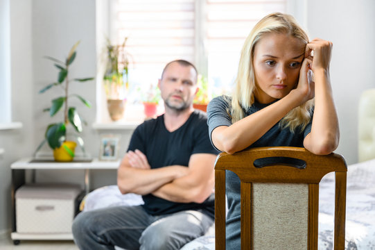 A portrait of a family conflict, the problems of a pretty blonde girl, a young woman in a gray sweater and an adult man, are sitting on a sofa in the room. Dissatisfied, swearing.