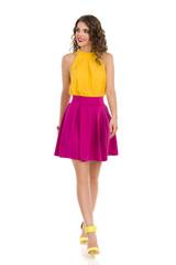 Walking Young Woman In High Heels, Pink Mini Skirt And YellowTop. Front View.