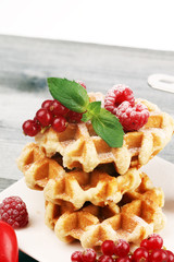 Traditional belgian waffles with fresh mint, sugar and raspberries on table