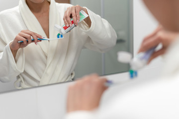 Woman in white bathrobe holding toothbrush, standing in bathroom
