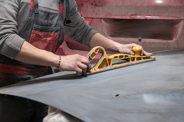 Man worker preparing for painting a car element using emery sender by a service technician leveling out before applying a primer after damage to a part of the body in an accident in vehicle workshop