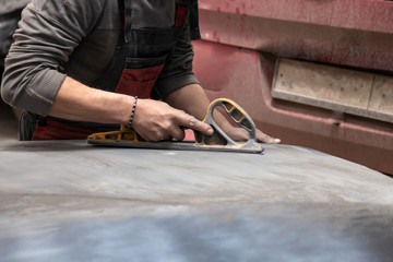 Man worker preparing for painting a car element using emery sender by a service technician leveling...