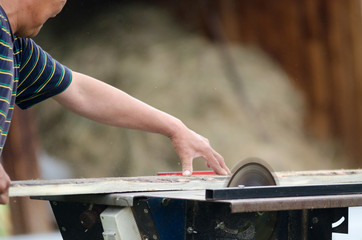A man neatly saws a Board on a circular saw against the background of a shed with wood.
