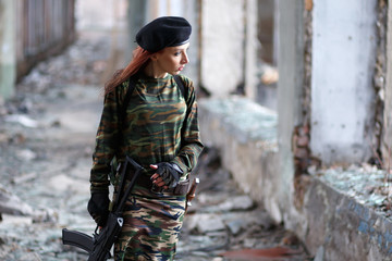 Soldier girl with weapons in camouflage uniform in a destroyed building. The concept of service in...