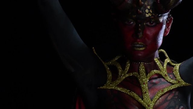 Scary red female demon with scaly skin and red eyes, is posing in the dark