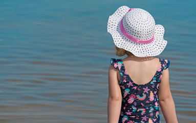Junges Mädchen steht am Strand und blickt aufs Wasser