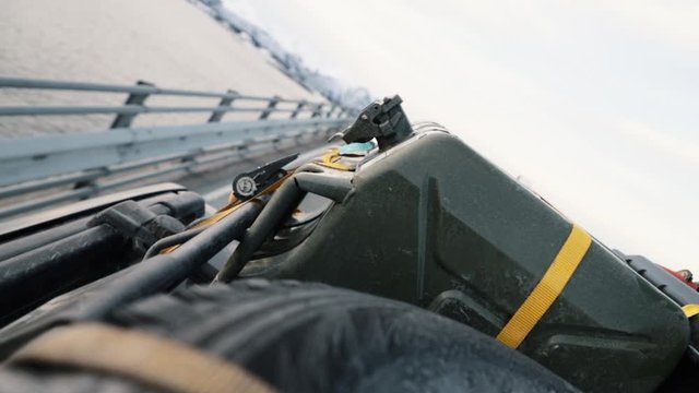 Driving vehicle with fuel can and spear tire tied down with ratchet strap and stretcher.