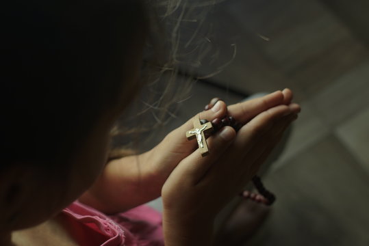 young girl prays with wooden rosary