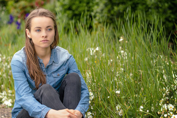 Emotion concept. A young unhappy woman sitting in a park. Burnout and depression.