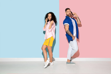 Fototapeta premium Young emotional caucasian couple in bright casual clothes posing on pink and blue background. Concept of human emotions, facial expession, relations, ad. Woman and man talking on phone, look busy.