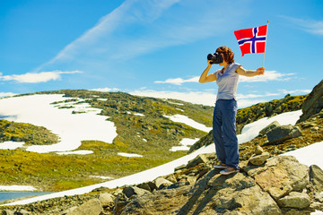 Obraz premium Tourist holds camera and norwegian flag in mountains