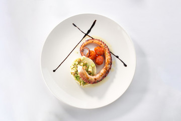 Grilled octopus with potatoes and tomatoes on white plate isolated on white background