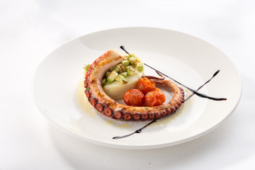 Grilled octopus with potatoes and tomatoes on white plate isolated on white background