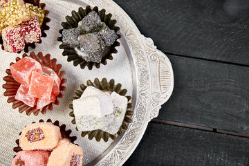 Set of various Turkish delight in traditional silver bowl on metal tray black background.Middle Eastern dessert. Top view. Flat lay
