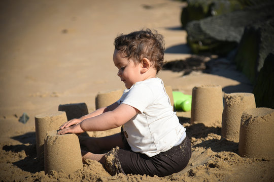 jeune enfant en train de réaliser un château de sable au bord de mer