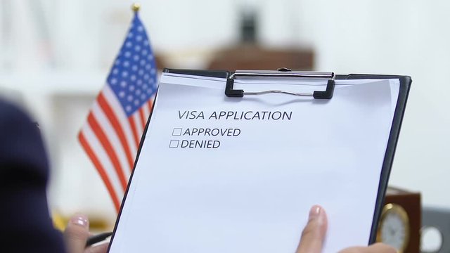 Female embassy worker checking US visa application, marking approved, permission