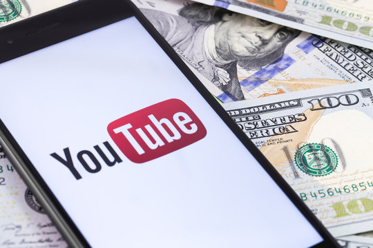 dollars banknotes and YouTube logo on the screen smartphone. YouTube is a free video sharing application that anyone can watch. Moscow, Russia - March 15, 2019